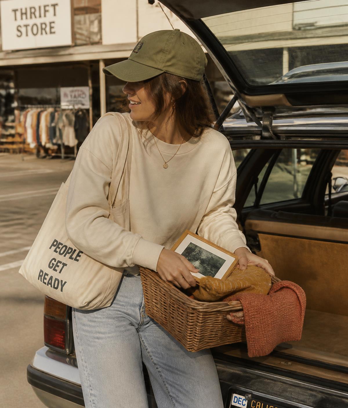 Woman in a cream crewneck loading thrifted finds into her car outside a thrift store